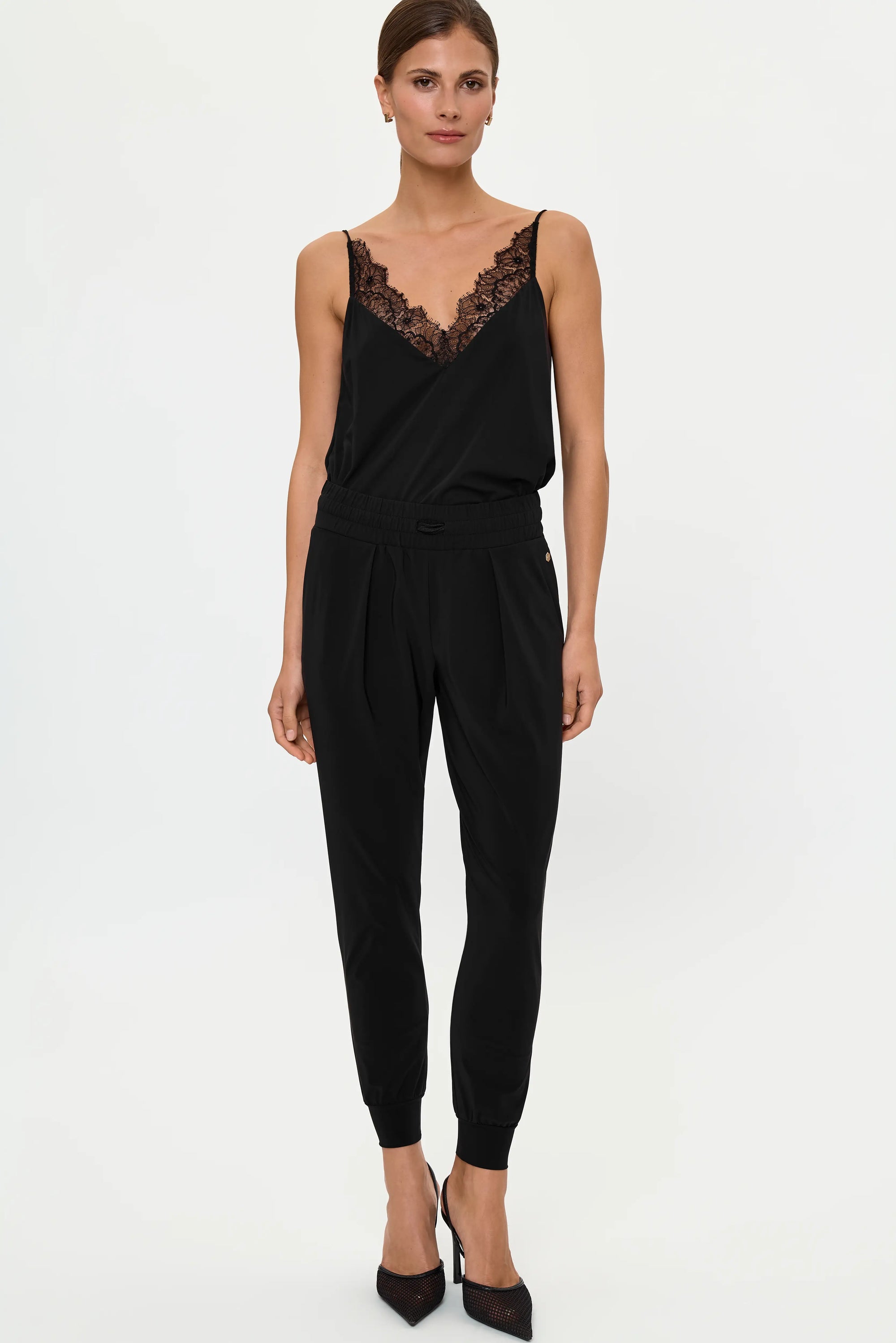 Model wearing black lace-trim camisole with black jogger pants and pointed heels.