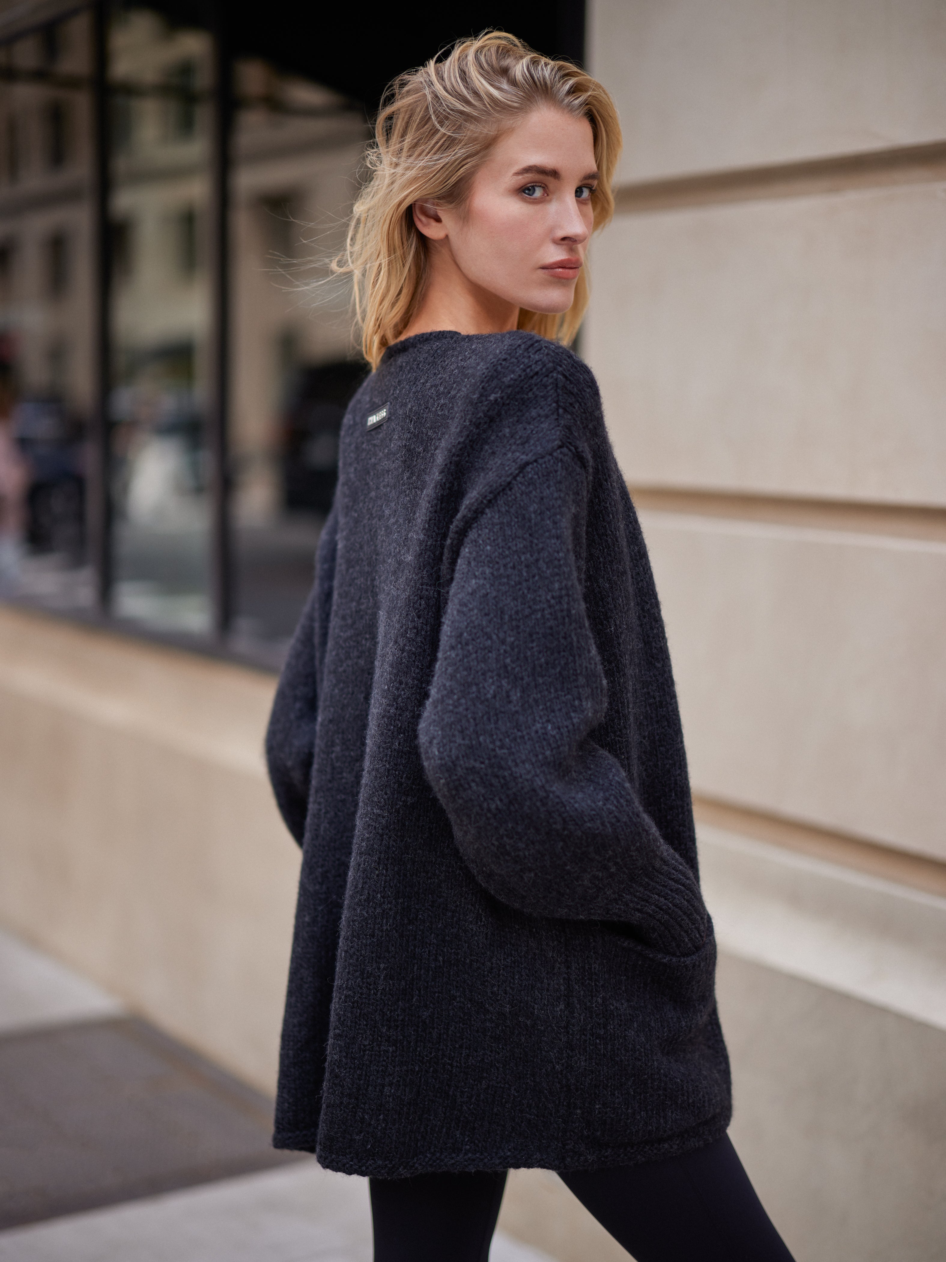 Blonde model wearing the black INA KESS oversized CANOLO sweater on a city street in NYC. 