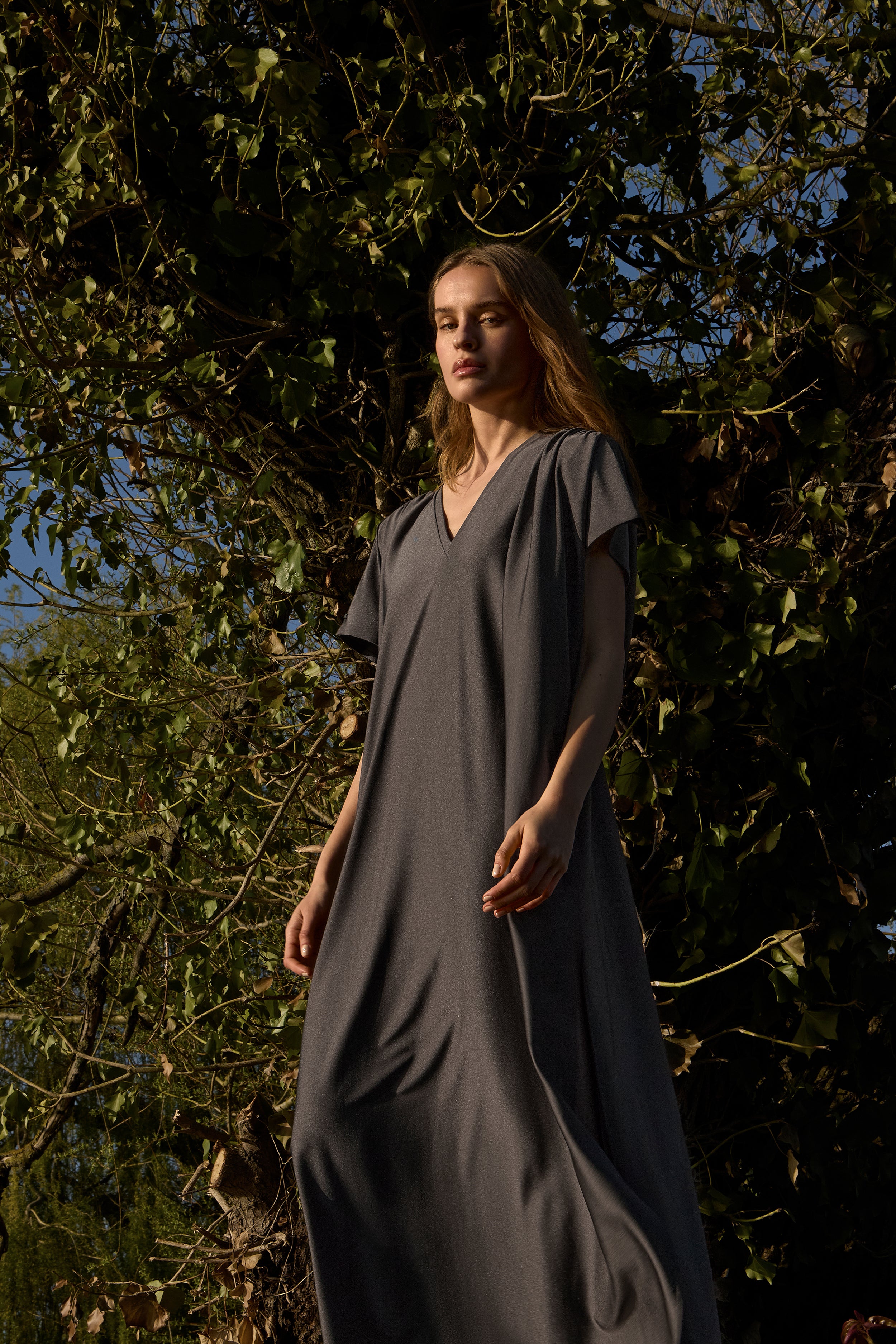 Woman in the INA KESS ETHERA dress in the colour ombre standing in front of trees with a blue sky background.
