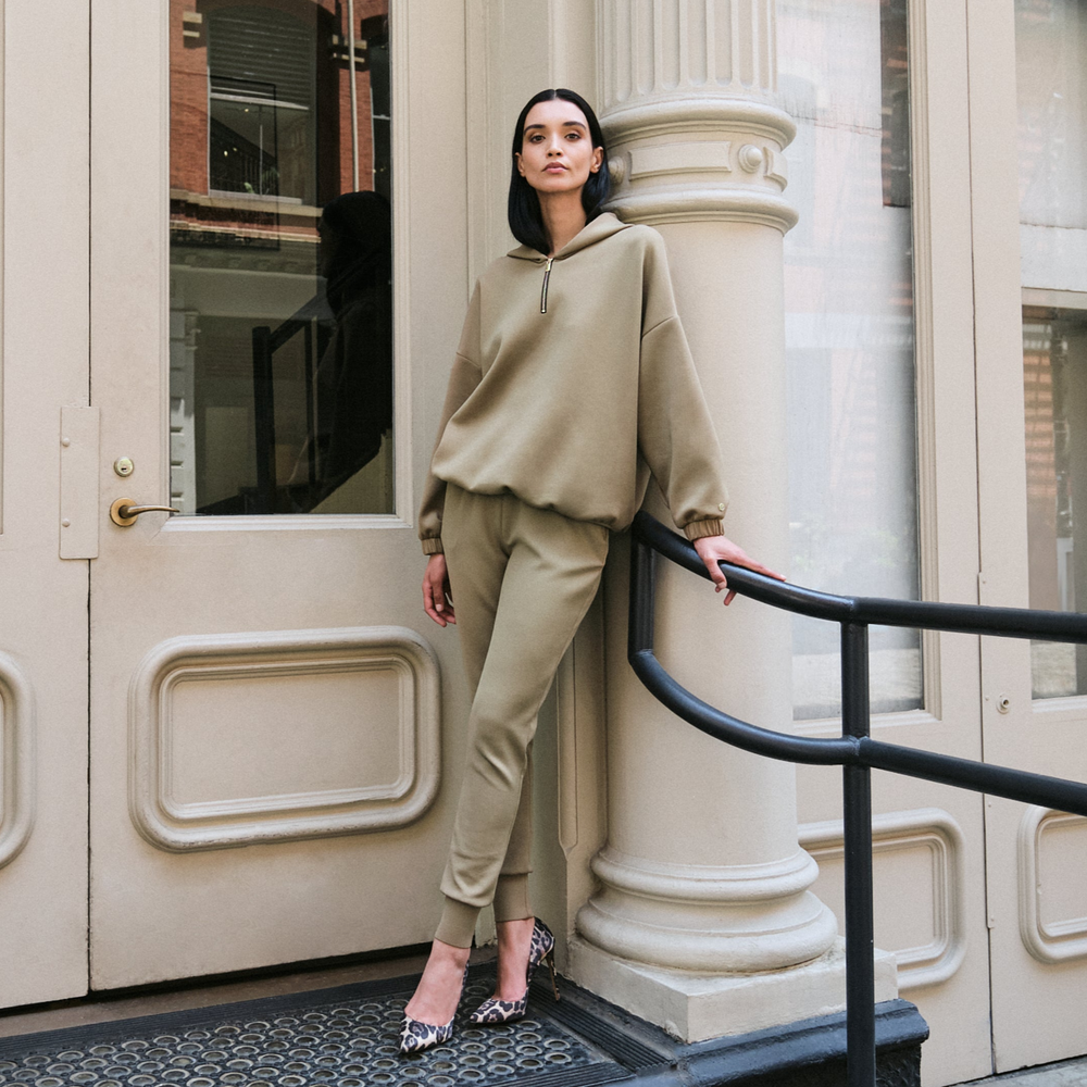 Model in a oliva coloured INA KESS Sweater and ROMULA Stretch Pants standing on a staircase in an urban setting