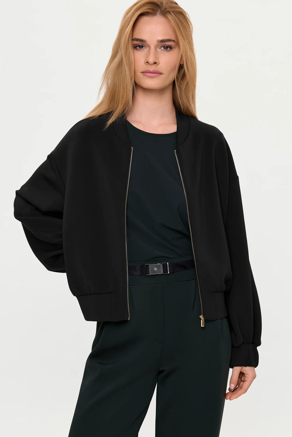 Model wearing black zip-front cardigan over forest green top with matching wide-leg pants.