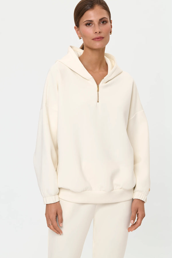 Model wearing ivory half-zip hooded sweatshirt with matching joggers, front close-up.