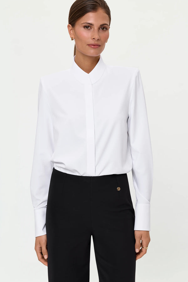 Front mid-length view of the white LEONTA shirt tucked into black LIORA pants, showing the crisp collar, long cuffs, and gold logo detail on the waistband.