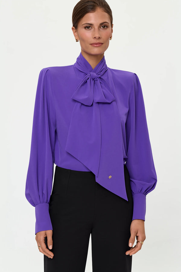 Model wearing a mystic purple tie-neck blouse with long balloon sleeves and black pants.
