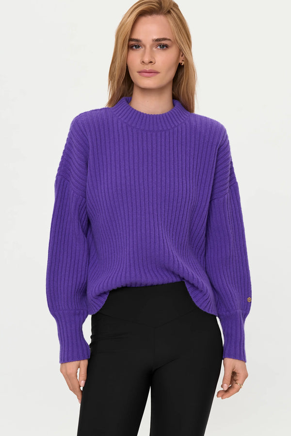 Model wearing mystic purple ribbed cashmere sweater with black high-waist flared pants, front close-up.