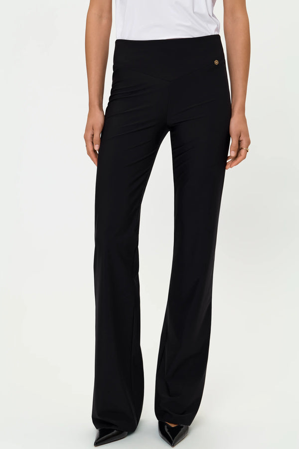 Model wearing black high-waist flared pants with white top and pointed heels, front view.