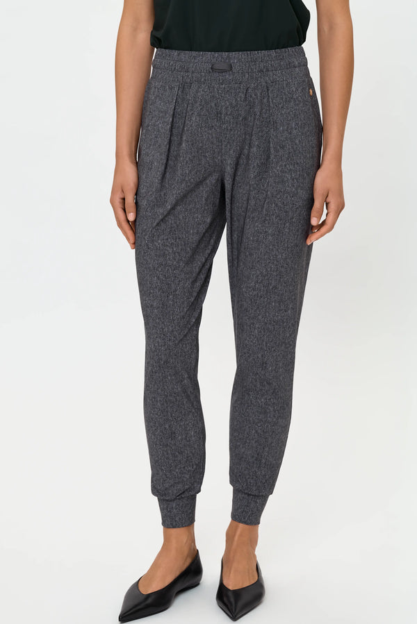 Front close-up of grey mica track pants showing pleated front, elastic waistband, tapered cuffs, and black flats.