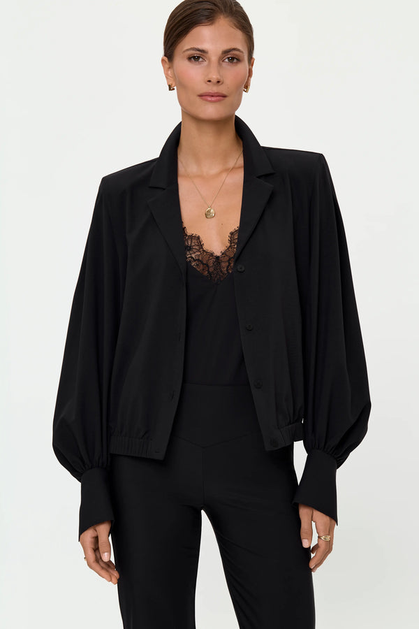 Mid-length front view of the VENTA Stretch Shirt in Black styled over the LUNARET lace-trim top and paired with LARIX Pants, highlighting the open neckline, soft drape, balloon sleeves, and monochrome layering.