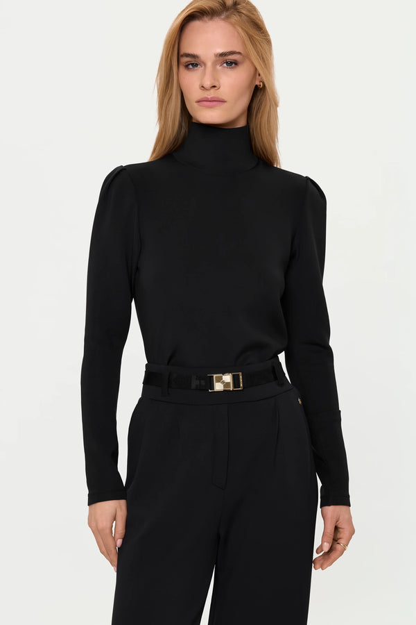 Mid-length front view of the LYNNIC Highneck Top tucked into SICANI Stretch Pants, highlighting the high neck, subtle shoulder volume, belt detail, and relaxed wide-leg tailoring.